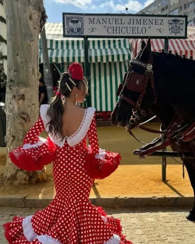 Traje de flamenca rojo de lunares blancos junto a un caballo de enganche, hecho por Sara, costurera en Sevilla Este